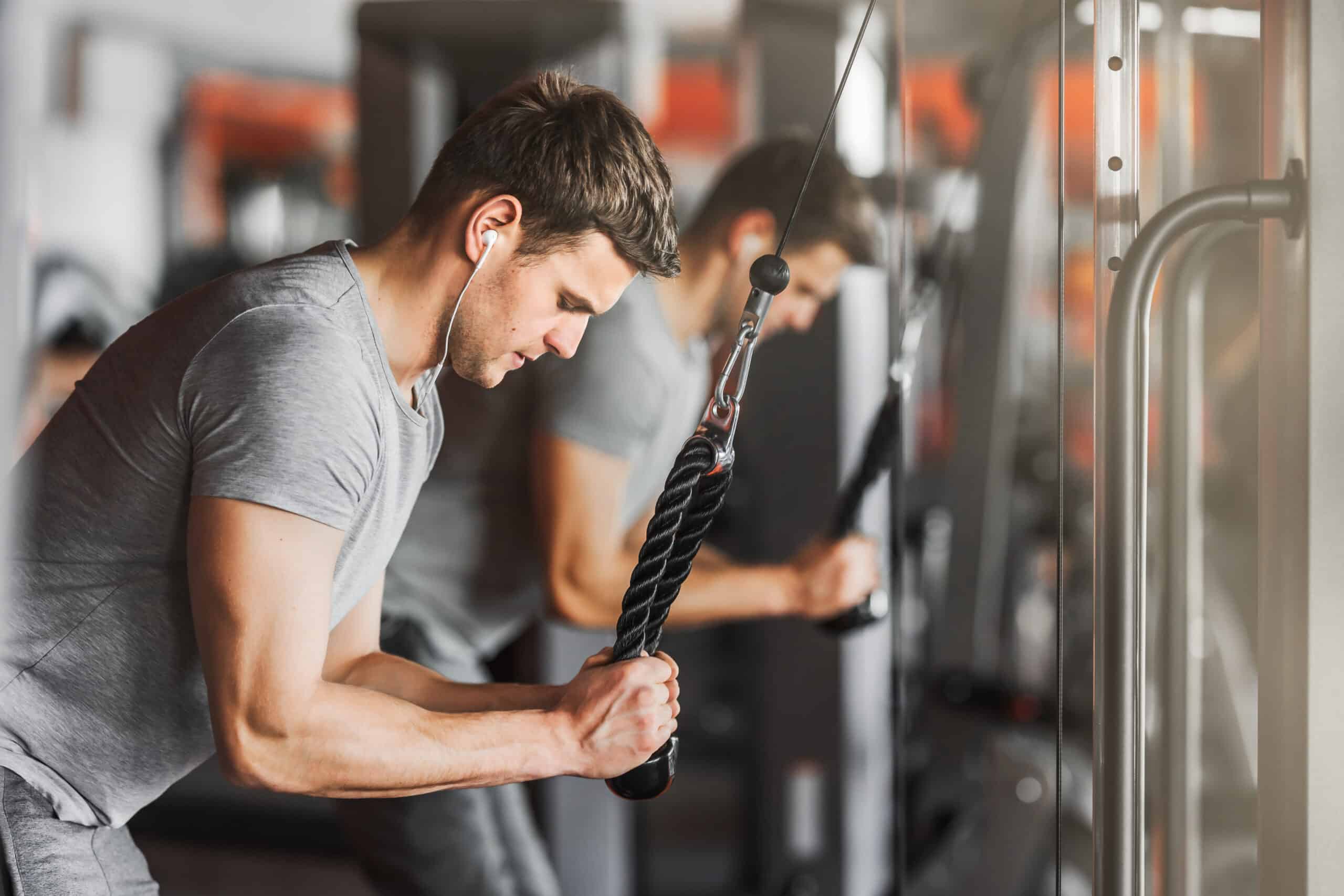 man doing tricep pulldowns in the gym wearing headphones