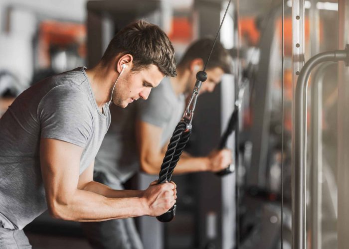 man doing tricep pulldowns in the gym wearing headphones